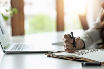 lady writing in a notebook in front of a laptop