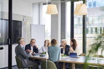 Business meeting held in light-filled glass meeting room.