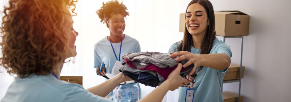 Volunteer handing a pile of clothes to be boxed to another volunteer.