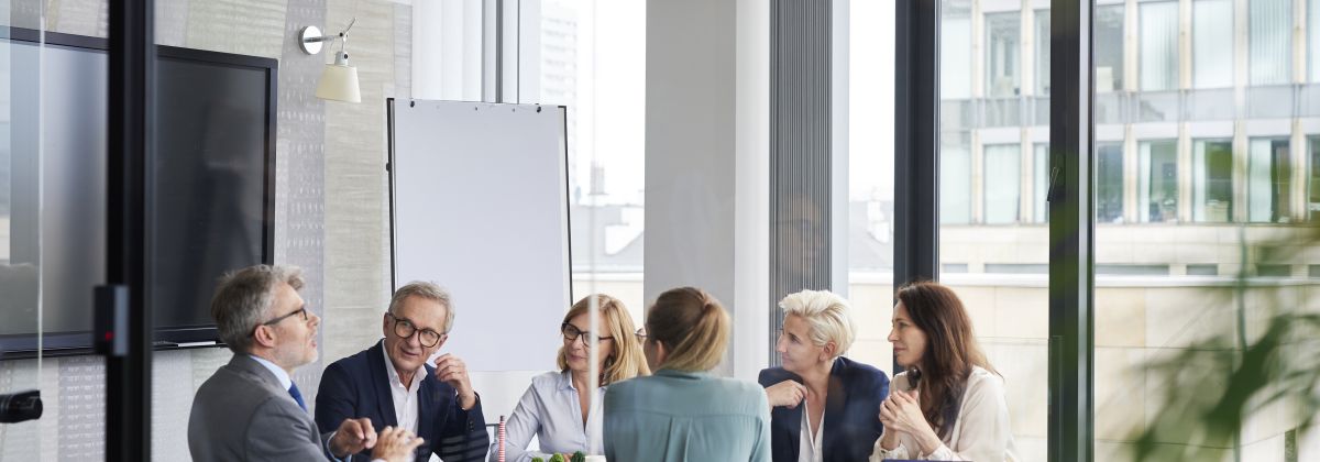 Business meeting held in light-filled glass meeting room.