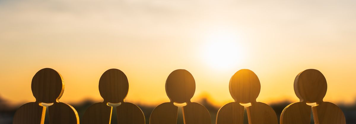 Wooden figures of businesspeople in a row with sunset in the background.